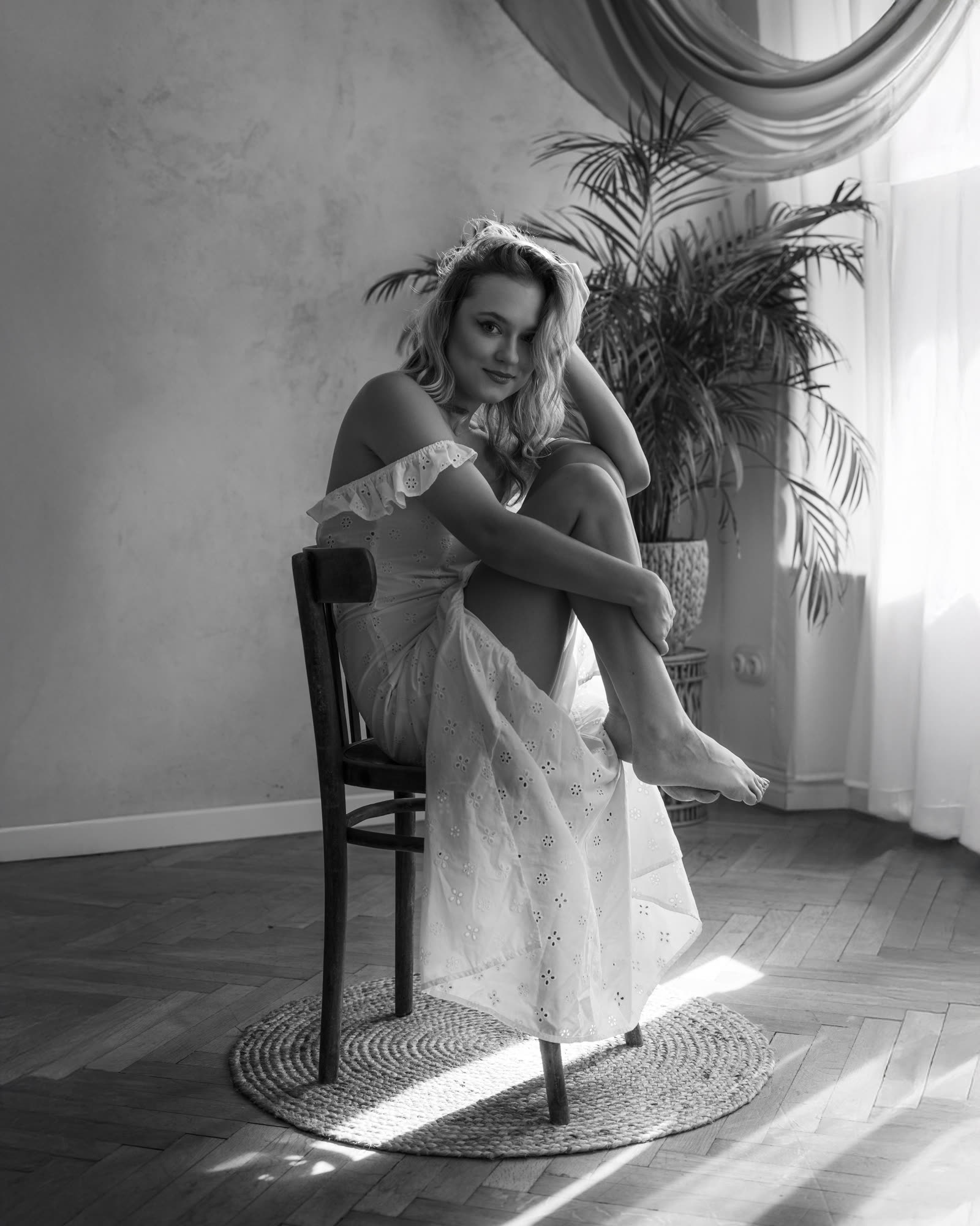 Czarno-biały portret w stylu vintage — kobieta w lnianej sukience na drewnianym krześle, atelierowe wnętrze